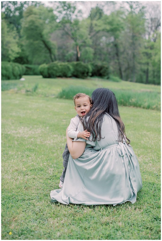 Mother In Green Dress Crouches Down And Hugs Her Little Boy