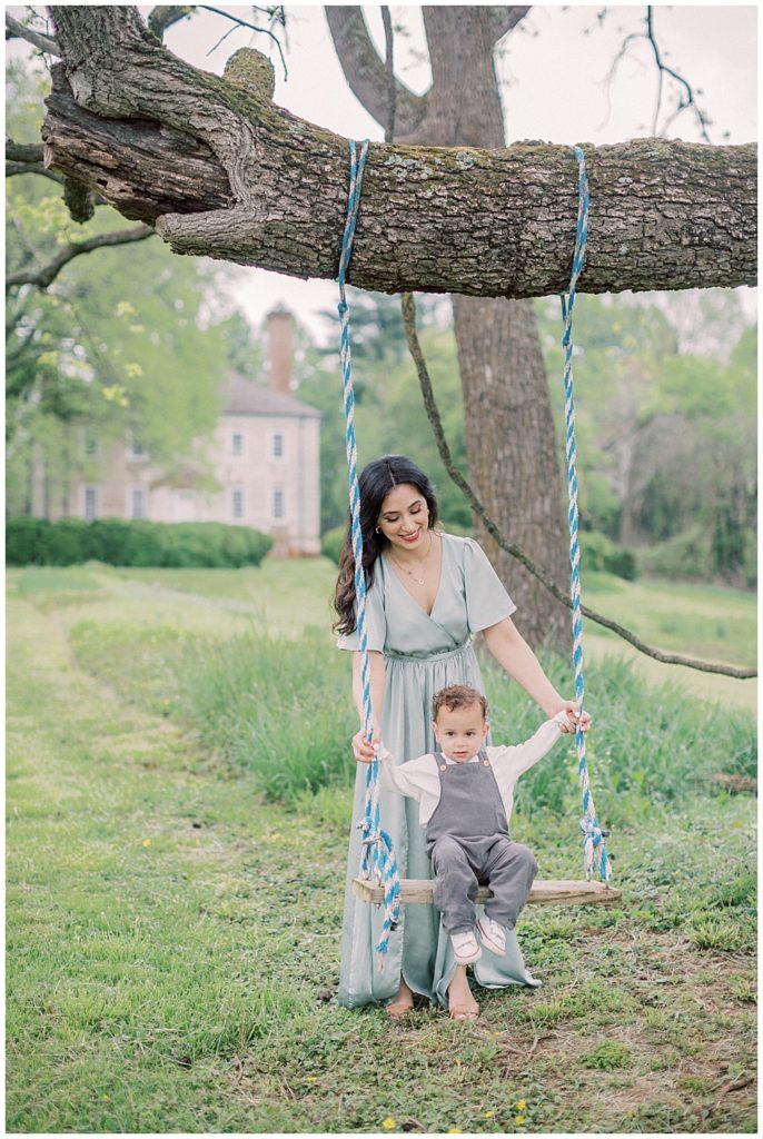 A Mother In A Green Dress Pushes Her Son In A Tree Swing At Salubria