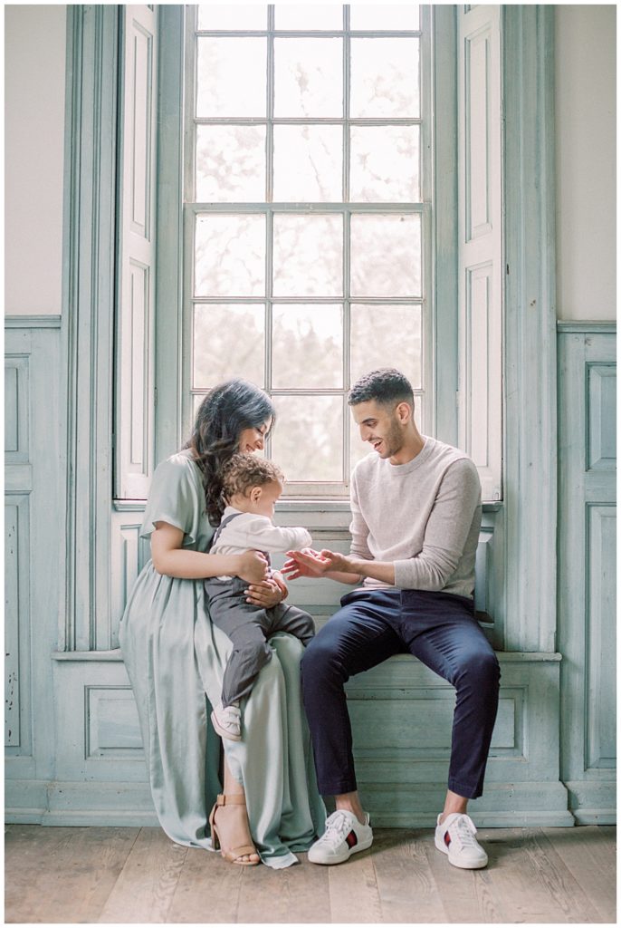 Mother, Father, And Toddler Son Sit In A Large Window During Their Elegant Family Photos At Salubria