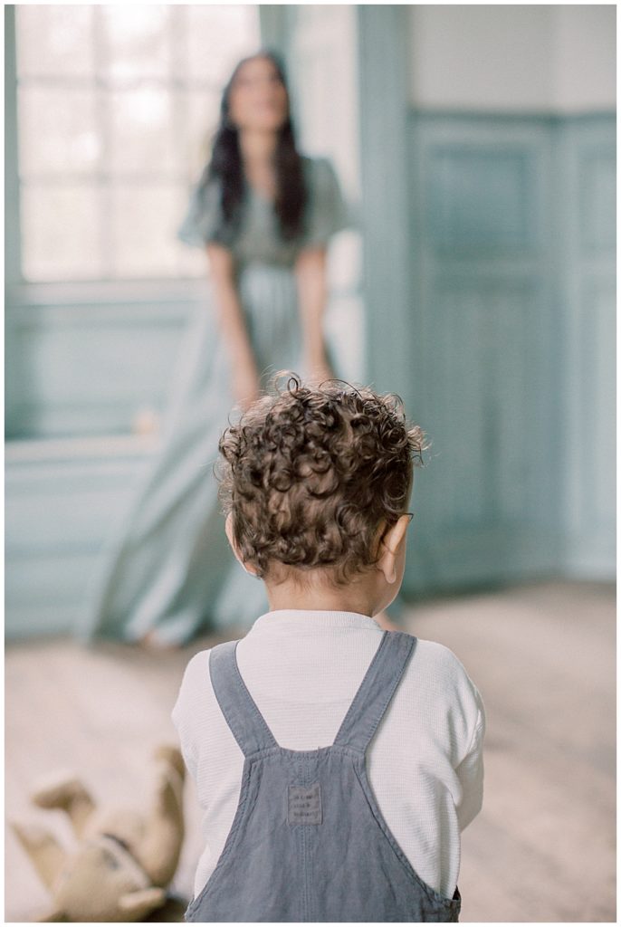 A little boy with brown curly hair walks towards his mother