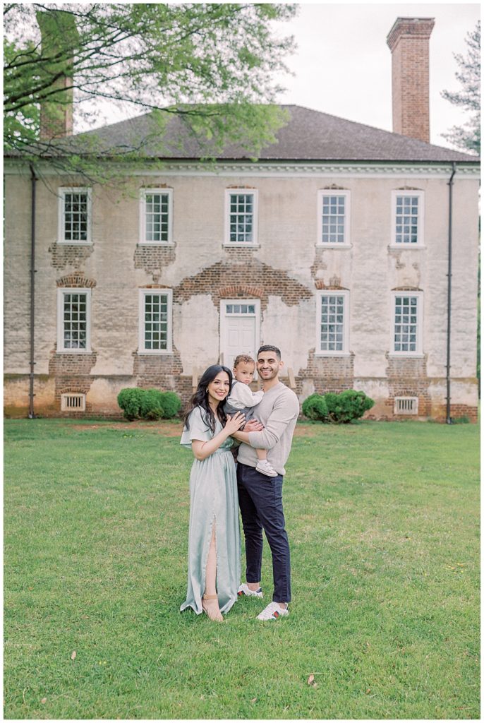 Mother and father stand in front of Salubria manor holding their toddler son