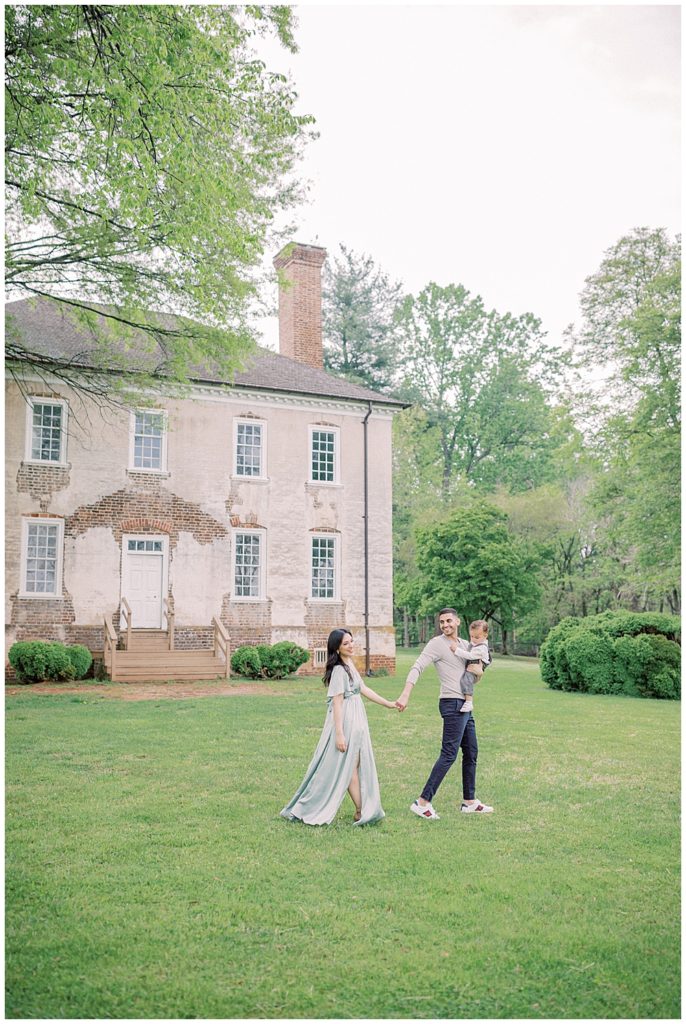 Mother and father walk holding hands while carrying their toddler son in front of Salubria Manor in Northern Virginia