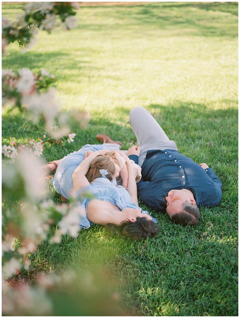 Mother And Father Lay In The Grass Holding Their Toddler Daughter