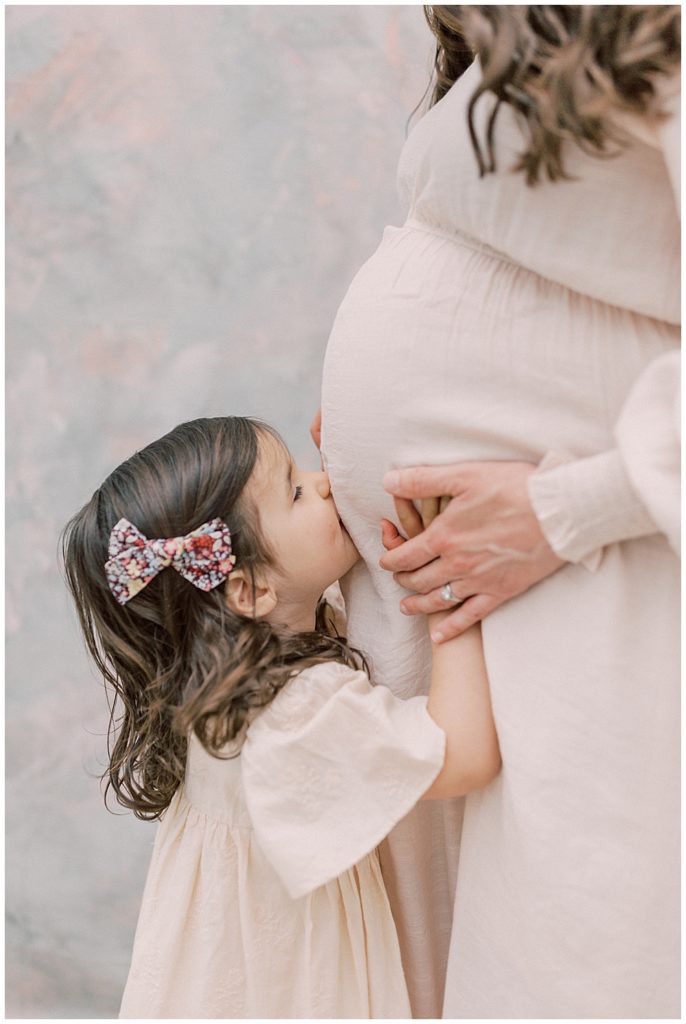 Little Girl Kisses Her Mother's Pregnant Belly During Their Maternity Studio Session With Daughter And Mother