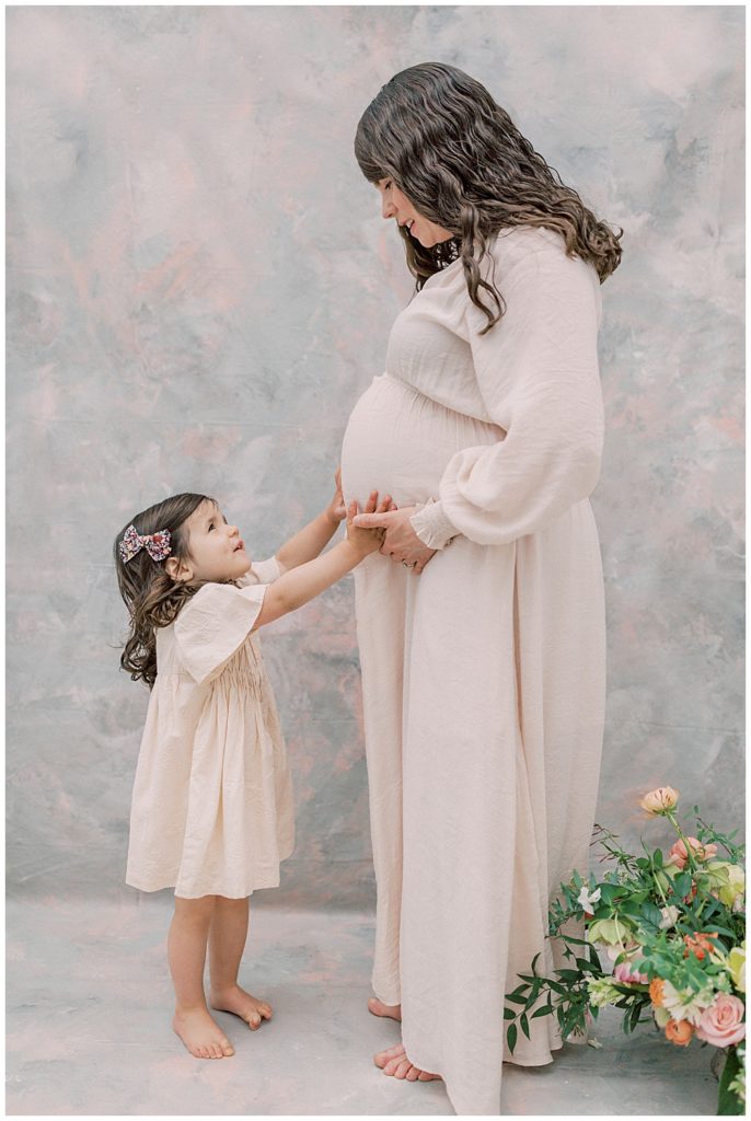 Little Girl Looks Up At Her Mother And Smiles While She Places Her Hands On Her Mom's Belly