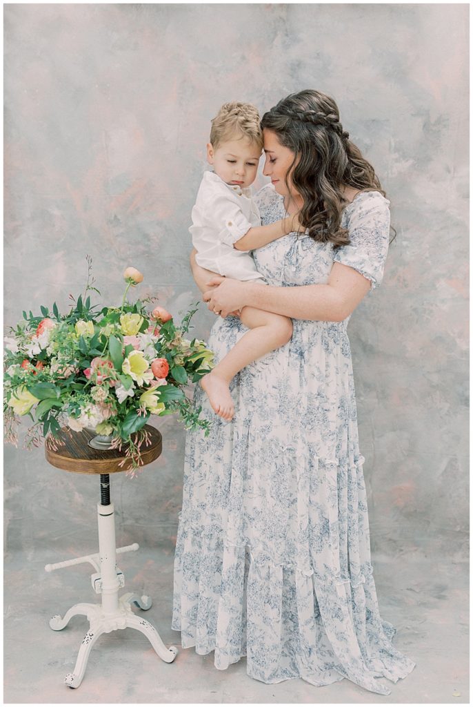 A Mother Holds Up Her Toddler Boy And Leans Into Him During Their Motherhood Session With Toddler