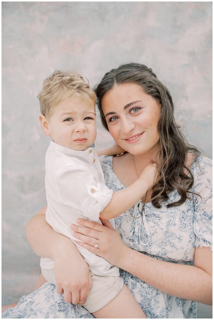 A Mother Holds Her Little Boy And Smiles During Her Studio Motherhood Session