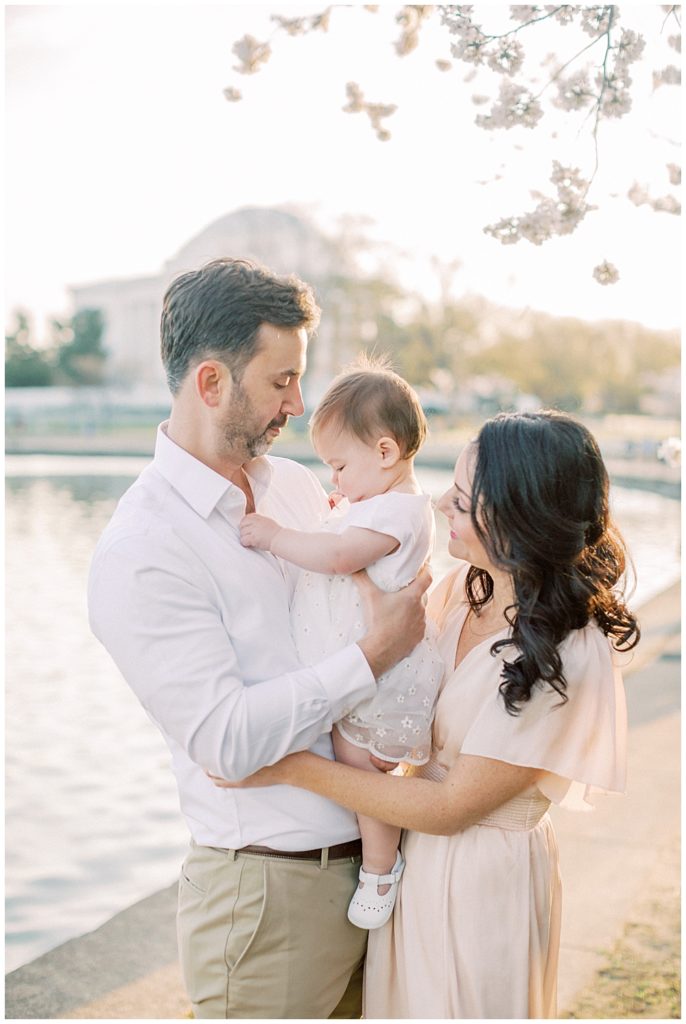 Mother And Father Hold Their Baby Daughter By The Tidal Basin At Sunrise