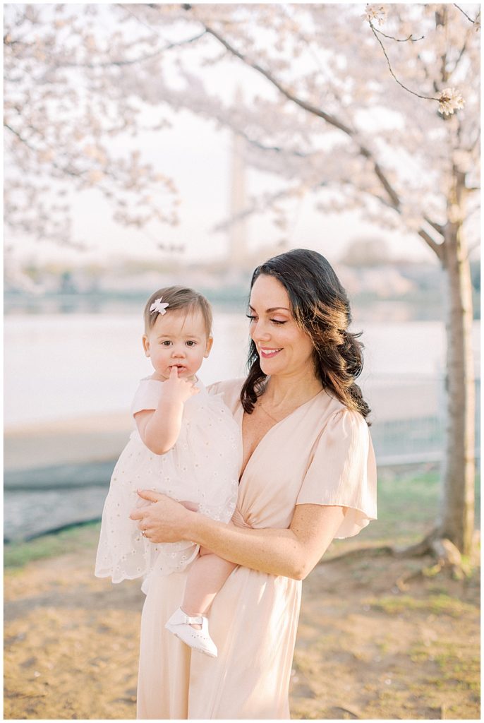 A Mother Holds And Smiles At Her Daughter While Standing In The Cherry Blossom Trees In Dc