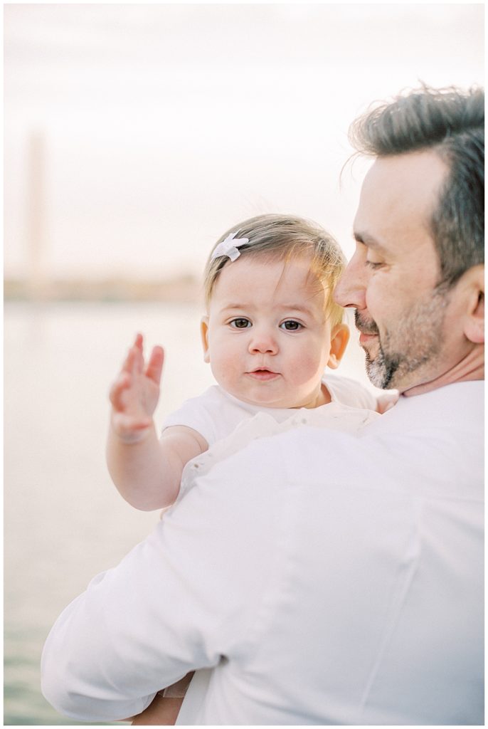 A Father Brings His Daughter Up To Him As She Looks And Smiles Over His Shoulder