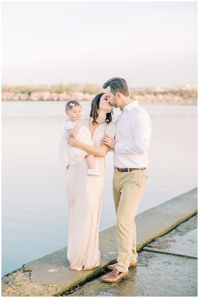 A Mother And Father Kiss While Standing Along The Tidal Basin During Peak Bloom