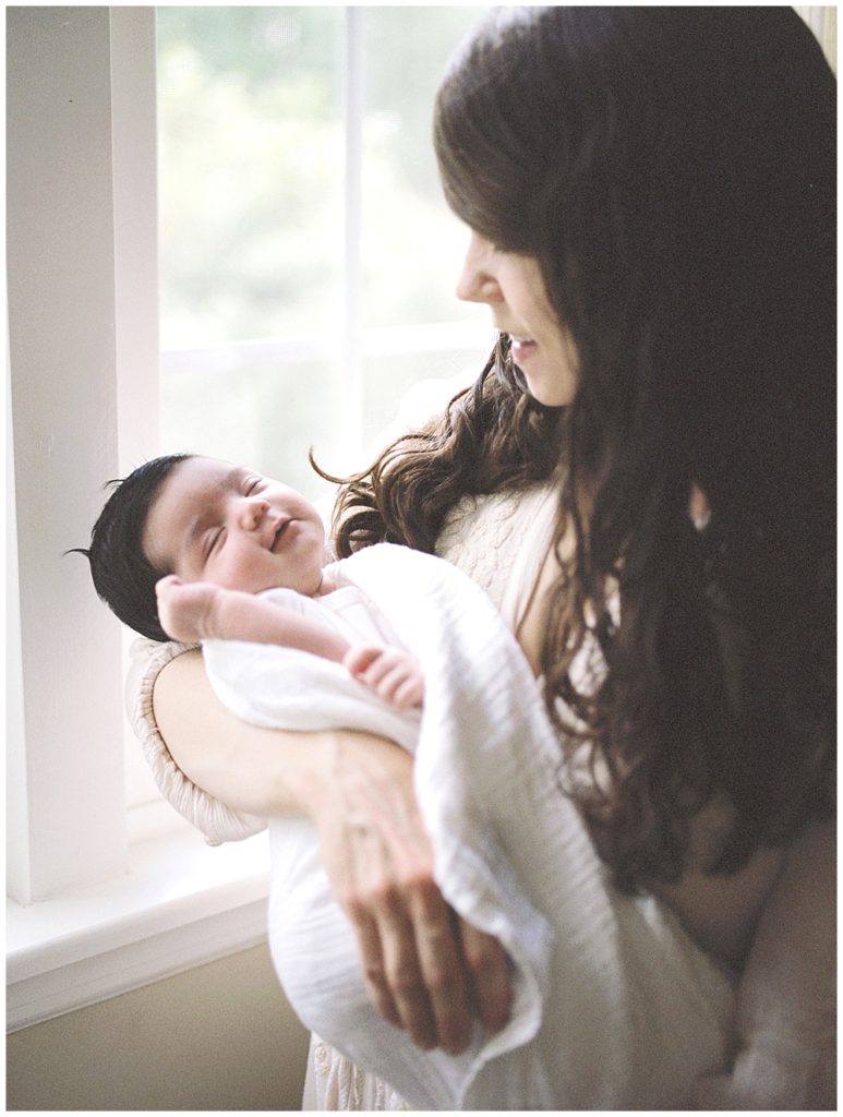 A Newborn Baby Held By Her Mother Smiles During Her Baltimore Newborn Session.