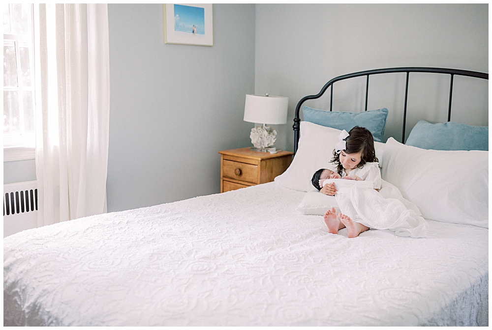 A Toddler Girl Holds Her Baby Sister On The Bed