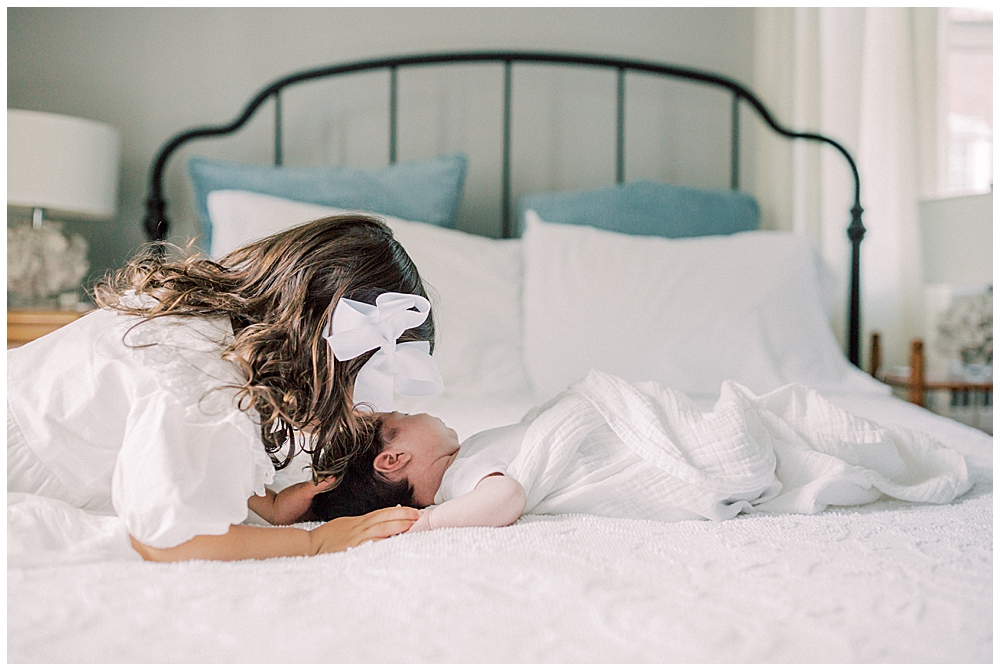 A Toddler Girl Leans Over Her Baby Sister, Kissing Her Head