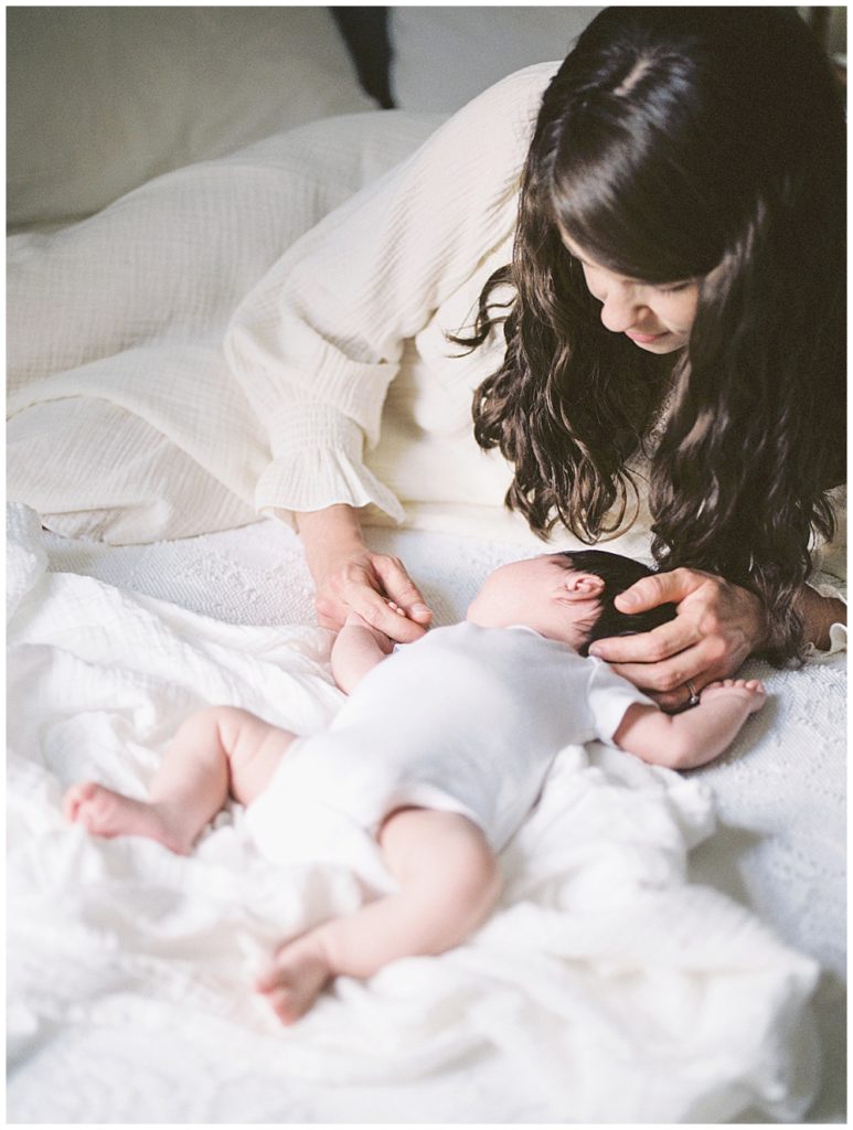 A Mother Cradles Her Infant Daughter's Head On The Bed