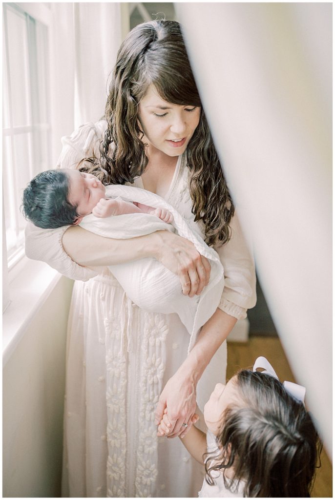 A Baltimore Newborn Session Where The Mother Holds The Baby And Leans Down To Talk To Her Toddler Daughter