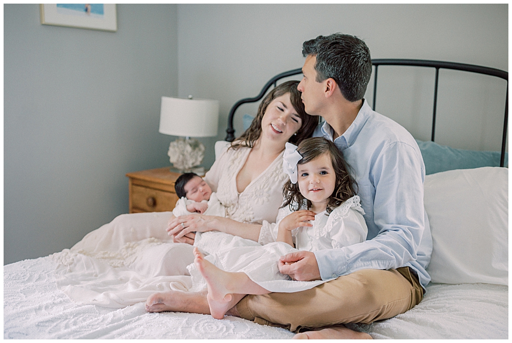 A Father Kisses His Wide's Head While Holding Their Daughters On The Bed