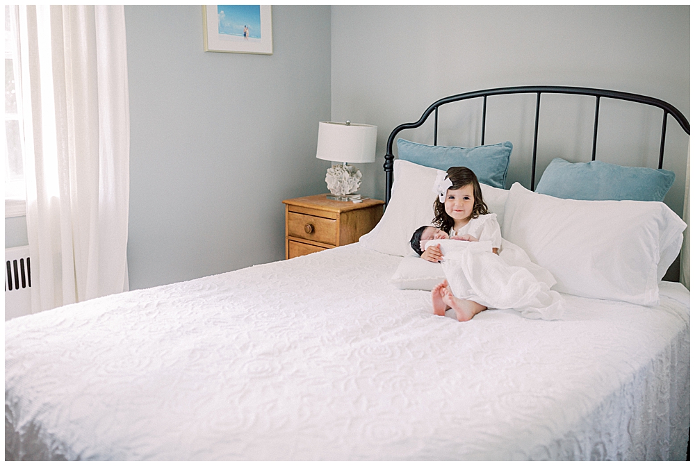 A Little Girl Holds Her Baby Sister On A Bed