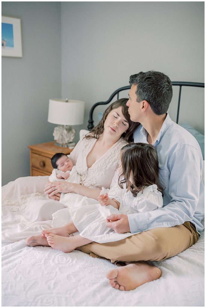 A Father Holds His Toddler Daughter And Kisses His Wife's Forehead During Their Baltimore Newborn Session