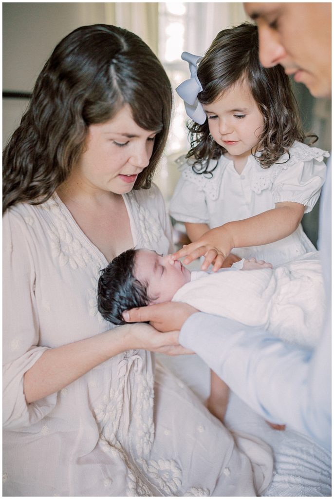 A Mother And Father Hold Up Their Toddler Daughter To Their Newborn Daughter During Their Baltimore Newborn Session