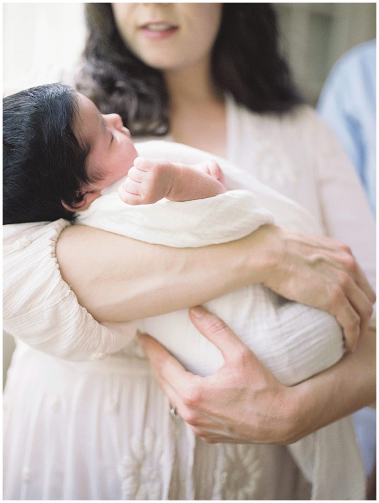 A Baby With Thick Brown Hair Is Held By Her Parents