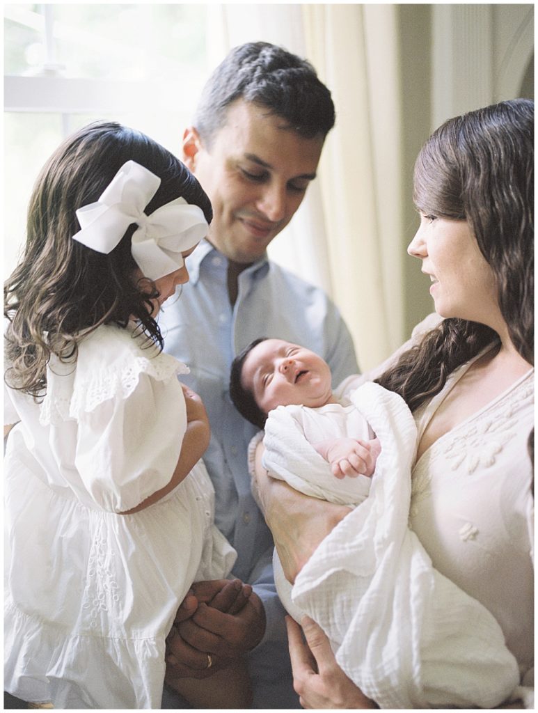 A Mother And Father Hold Their Newborn Daughter Up To Their Toddler Girl