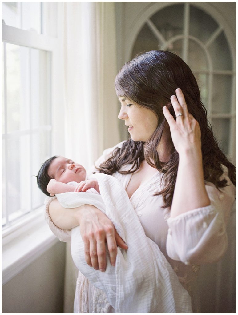 Mother Holds Her Newborn Baby And Tucks A Strand Of Hair Behind Her Ear.