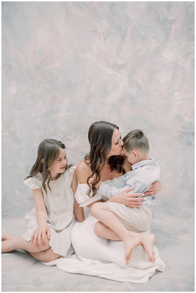 A Mother Sits On The Floor With Her Son And Daughter, Hugging Her Son