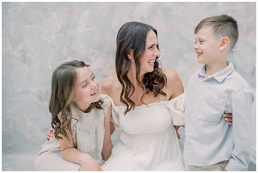 A Mother Sits On The Floor, Smiling At Her Son And Daughter