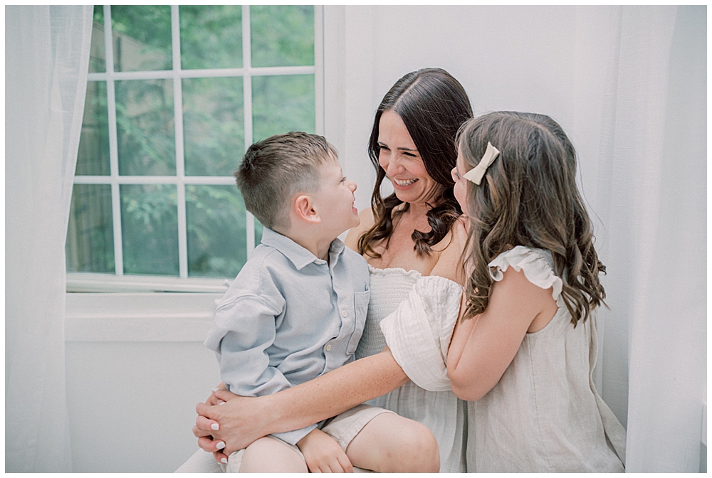 A Mother Smiles Her Her Son While Holding Him And Embracing Her Daughter