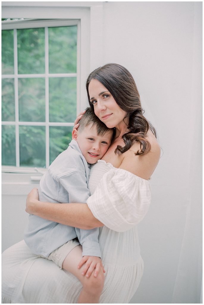 A Mother With Brown Hair Holds Her Young Son On Her Lap Looking At The Camera