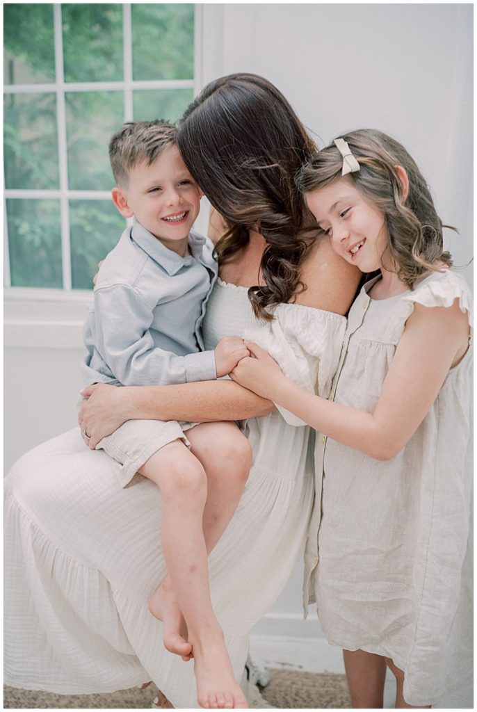 A Mother Holds Her Young Son While Her Daughter Stands Behind Her Embracing Her