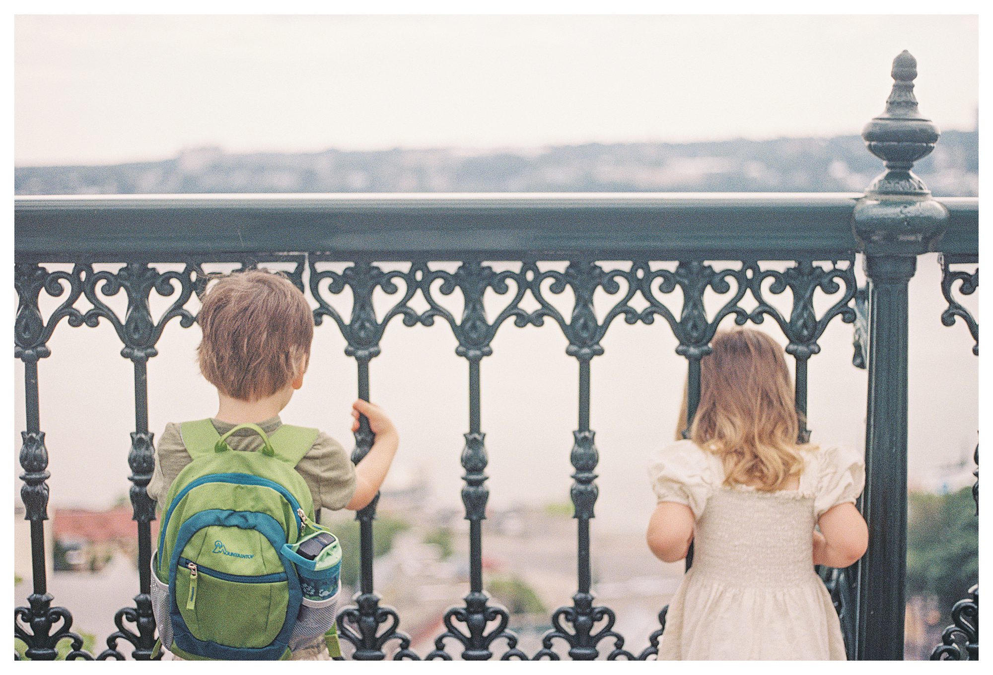 Two Children Look Through Iron Fence In Quebec City.