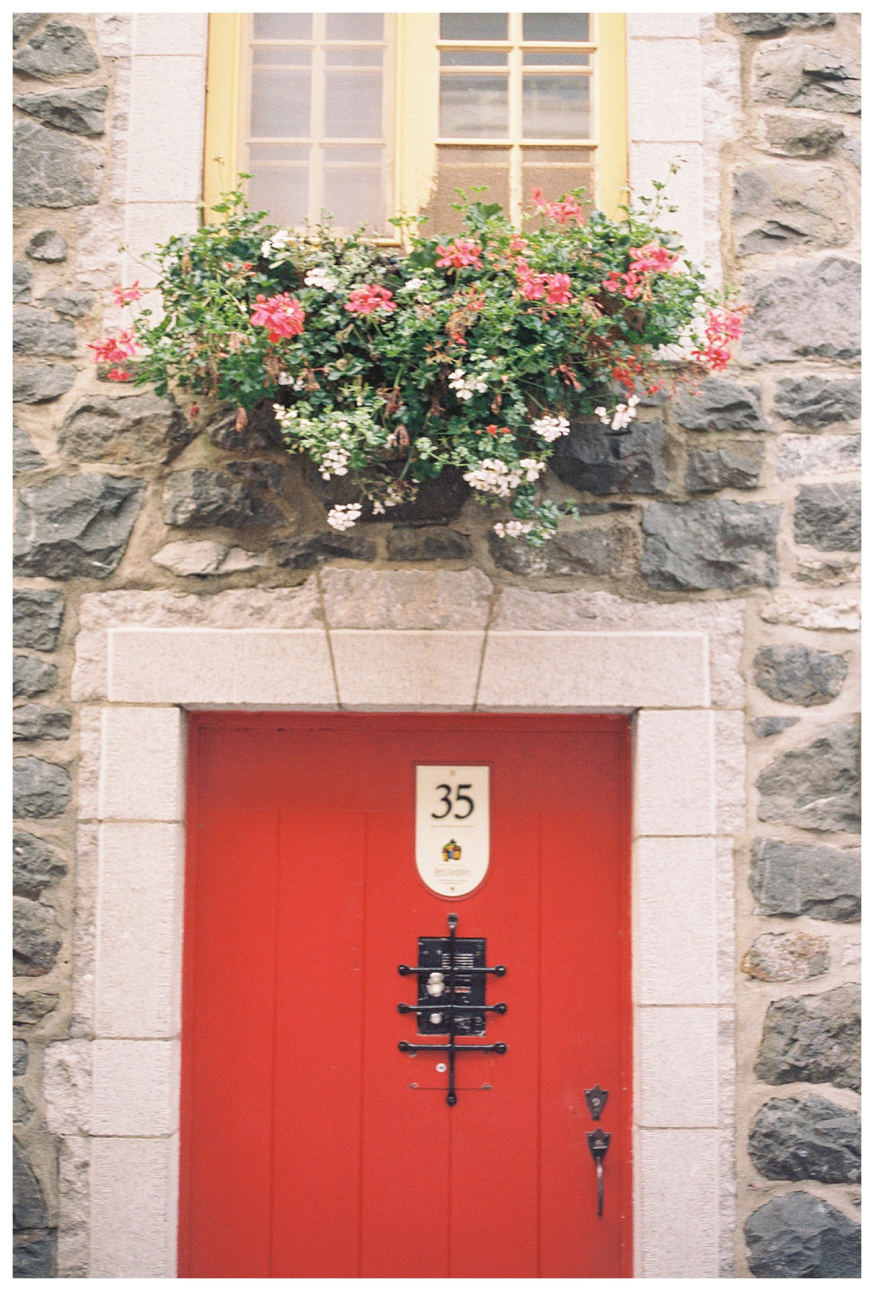 A Red Door On A Stone Building With Flower Window Boxes.