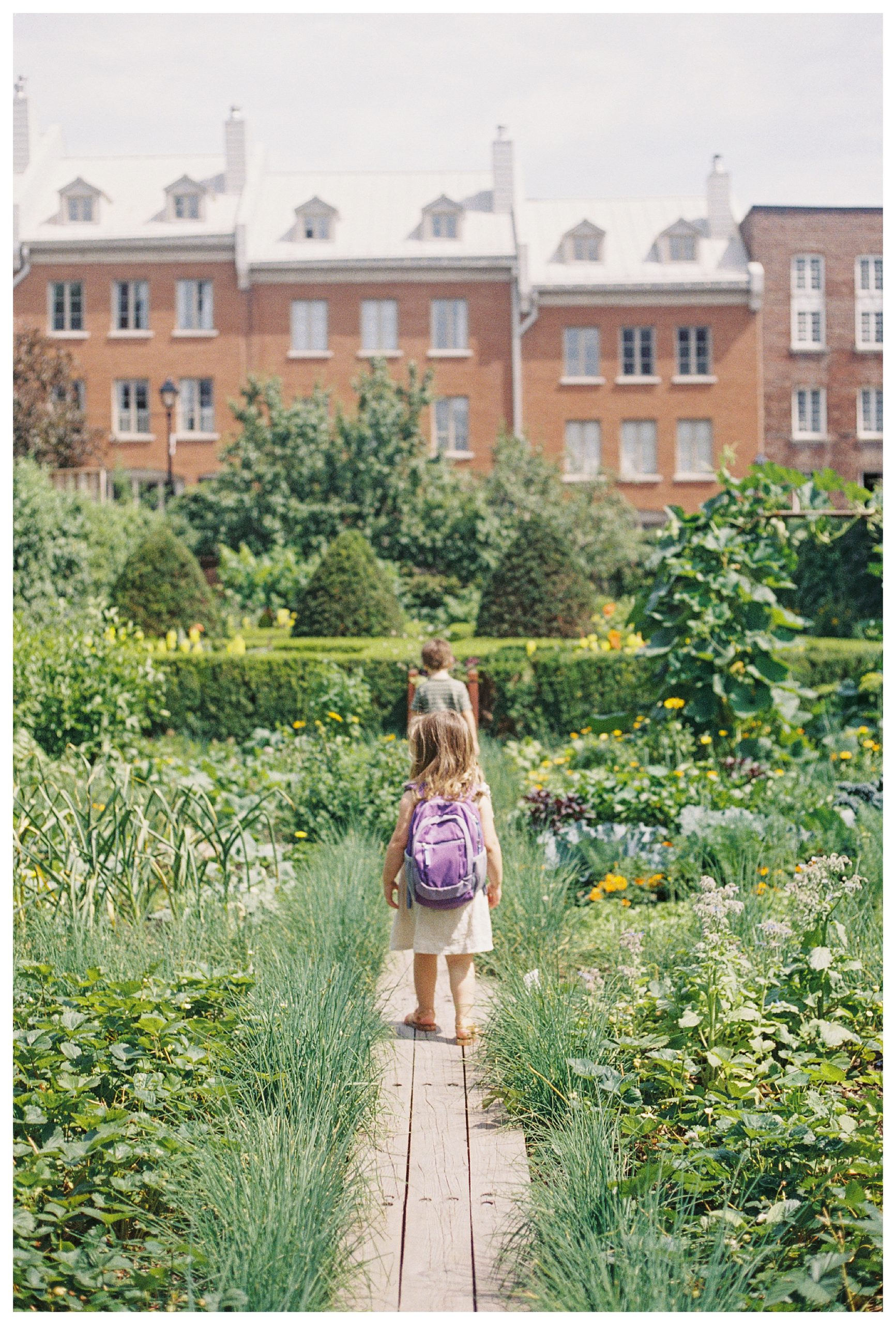 Two Children Walk Along A Wooden Path In A Garden In Montreal, Canada