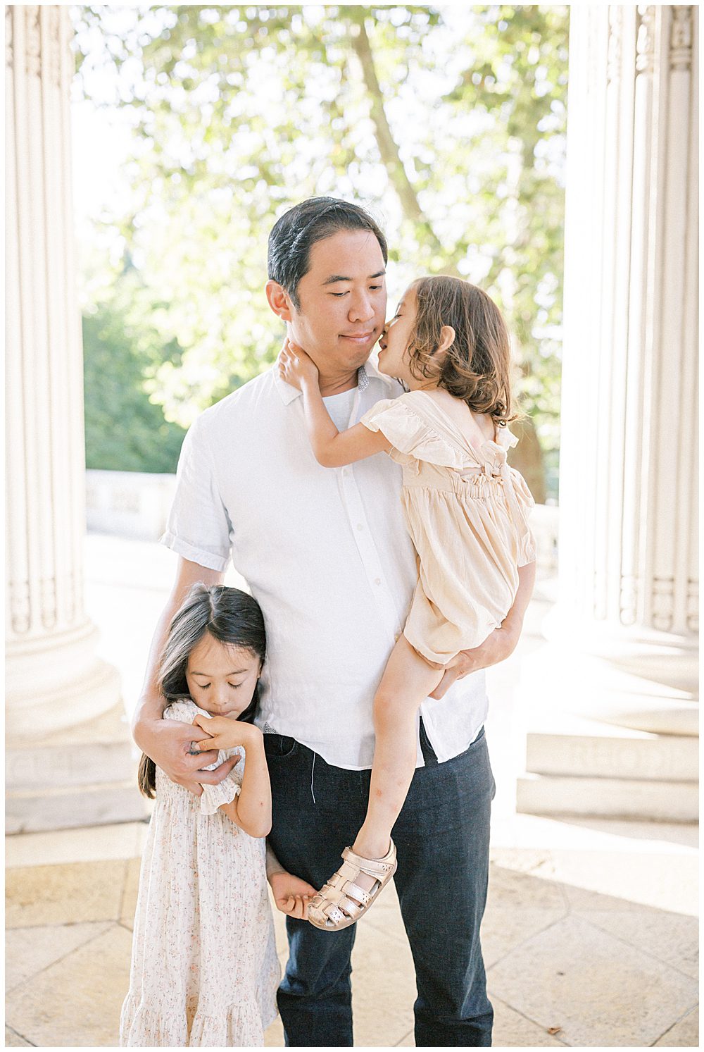 Father Holds One Young Daughter While His Other Daughter Stands Next To Him.