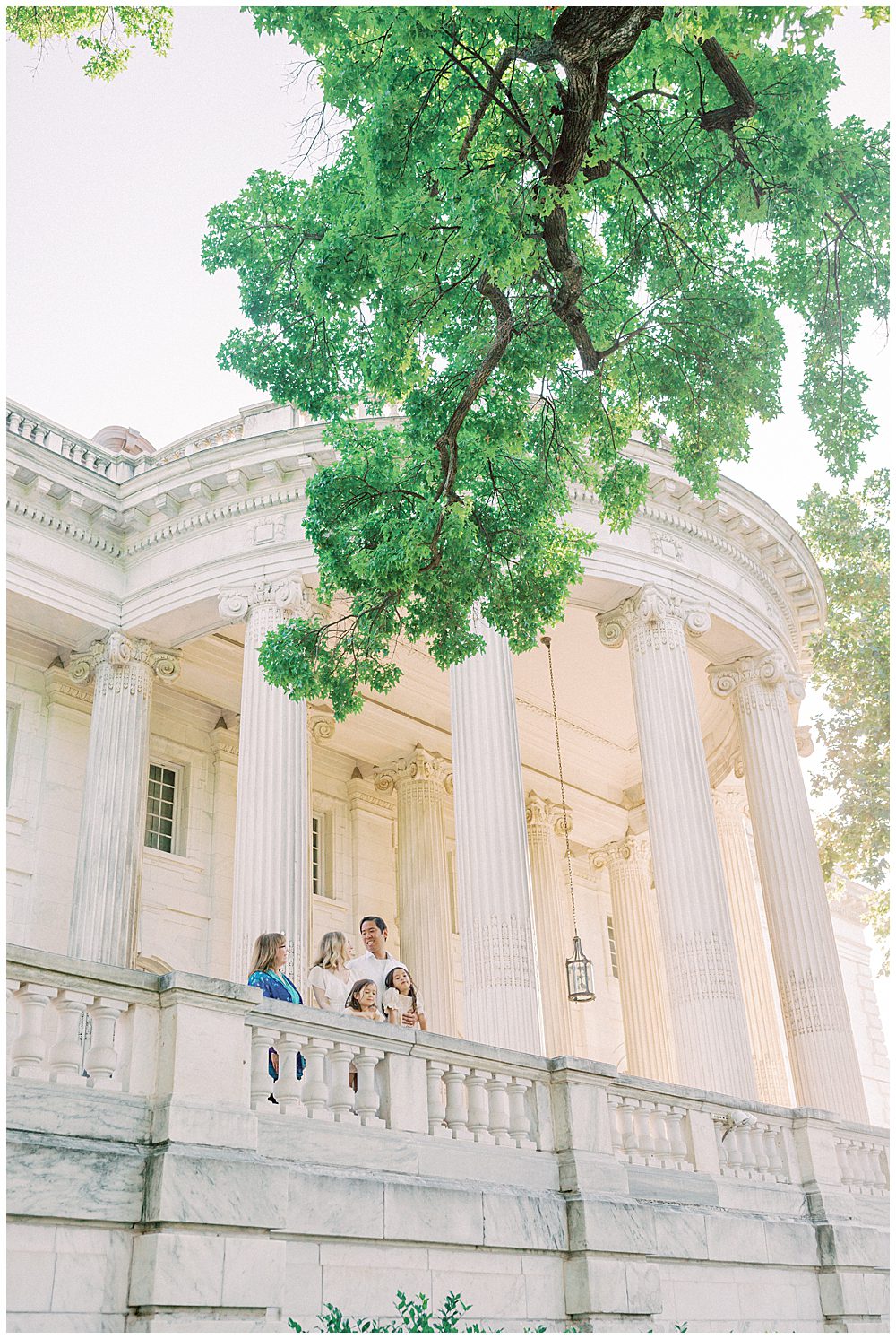 Mother, Father, Two Young Daughters, And Grandmother Stand At Dar Constitution Hall By The Columns Smiling At One Another.