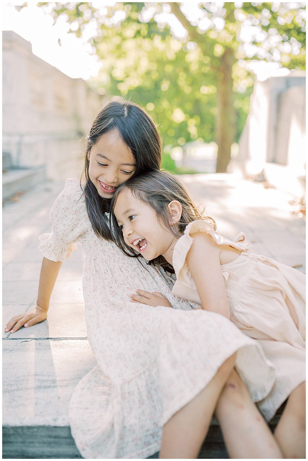 Two Young Sisters Sit On Steps At Dar Constitution Hall And Lean Into One Another Laughing.