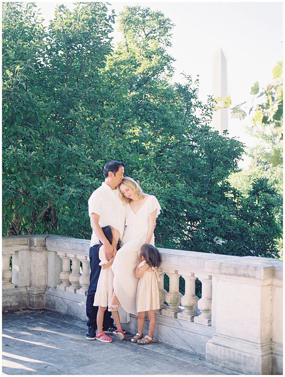 Blonde Mother Sits On The Ledge At Dar Constitution Hall With Her Husband And Two Young Daughters During Their Dar Constitution Hall Family Session.