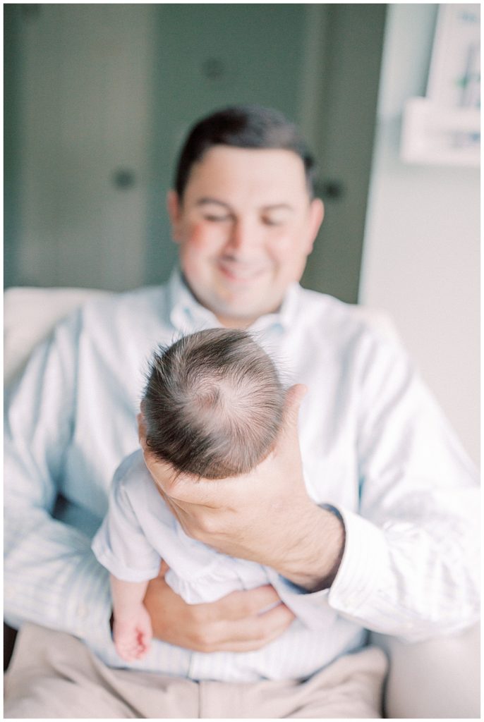 View. Of Fuzzy Brown Newborn Hair On Baby Held By His Father Smiling Down At Him.