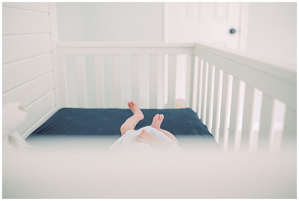 Baby Toes Stick Up From Outside A White And Navy Crib.