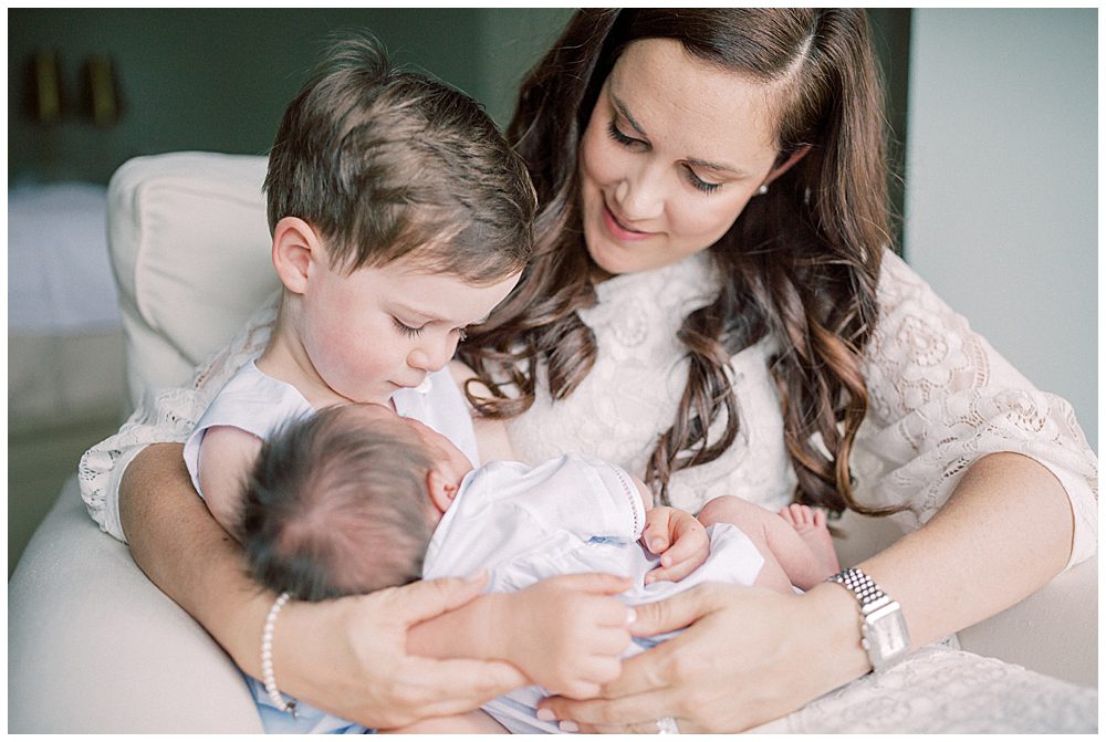 Little Boy Looks Down At His Newborn Brother Held By His Mother.