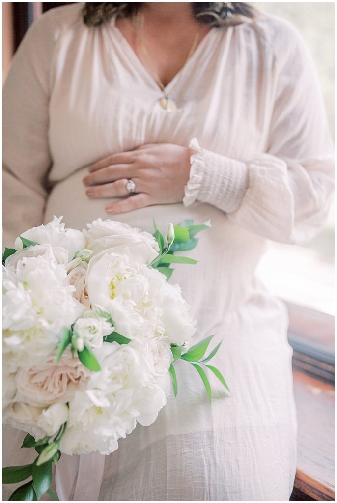 Pregnant Belly With Mom's Hand On Top Of The Belly And One Hand Holding A White Bouquet Of Roses