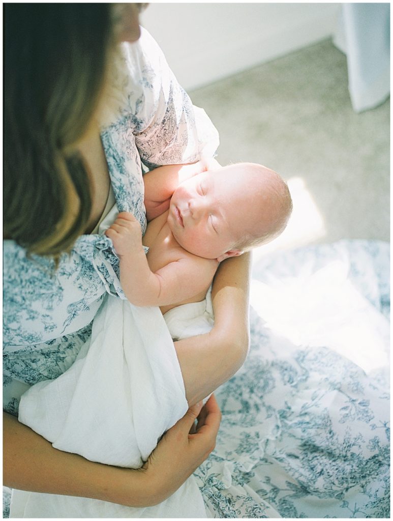 Newborn Baby Held By His Mother While She Sits In Front Of A Window.