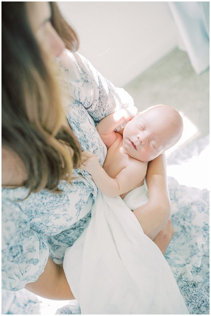 Baby Boy Is Held By His Mother In Front Of A Window.