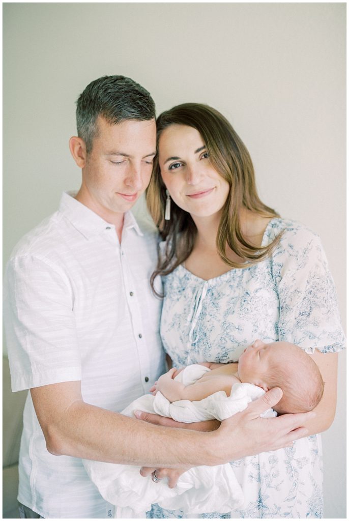 Mother Holds Her Newborn Baby And Leans Into Her Husband While Looking At The Camera During Their Joint Base Andrews Newborn Session.