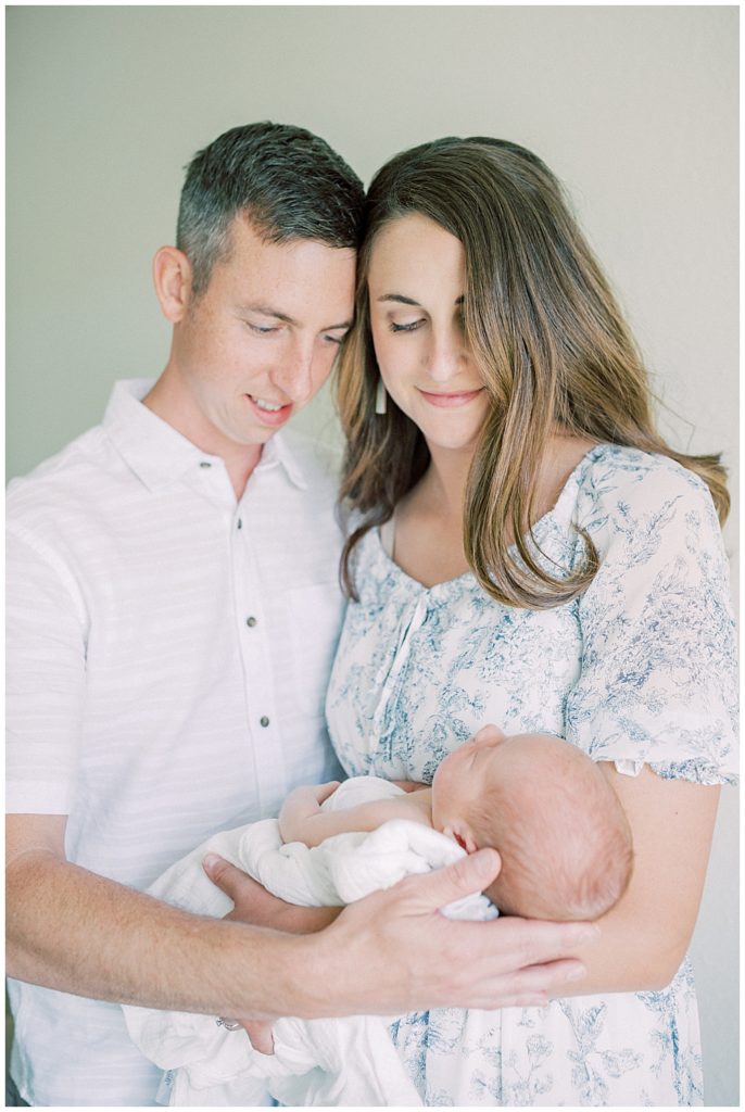 Mother And Father Lean Into One Another While Holding Their Newborn Baby During Their Joint Base Andrews Newborn Session.