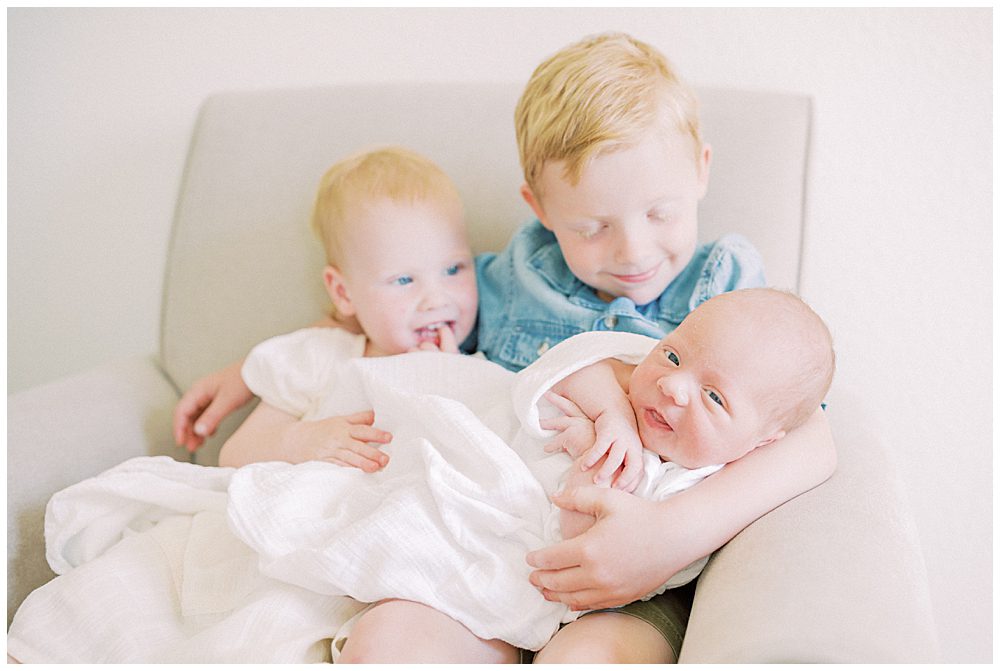 Red Haired Big Brother And Sister Hold Their Baby Brother On Their Lap