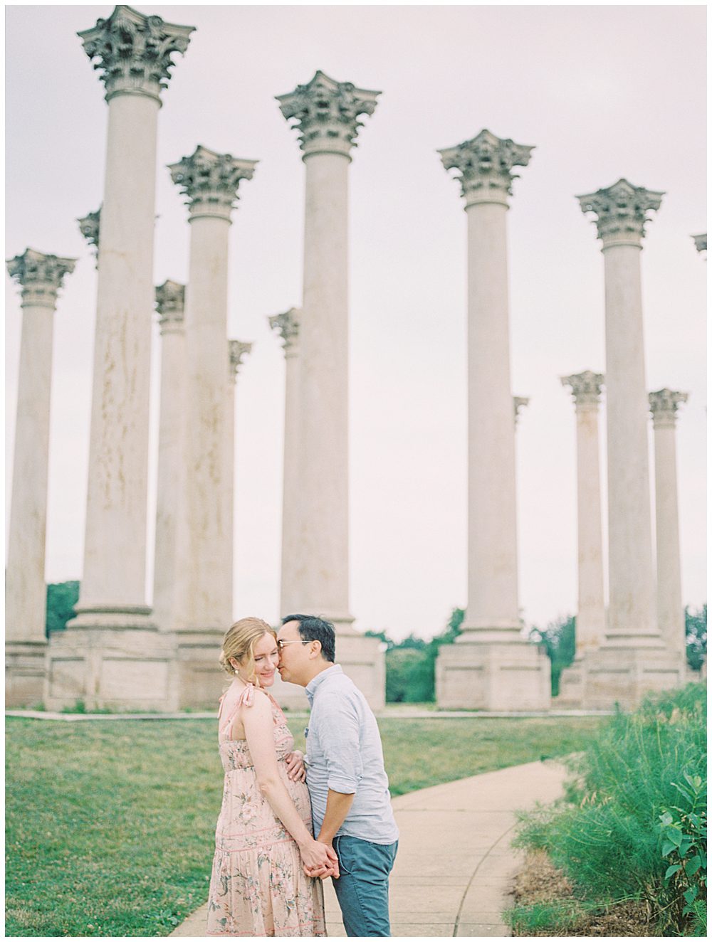 Husband Leans Over To Kiss His Wife's Cheek During Their National Arboretum Maternity Session.