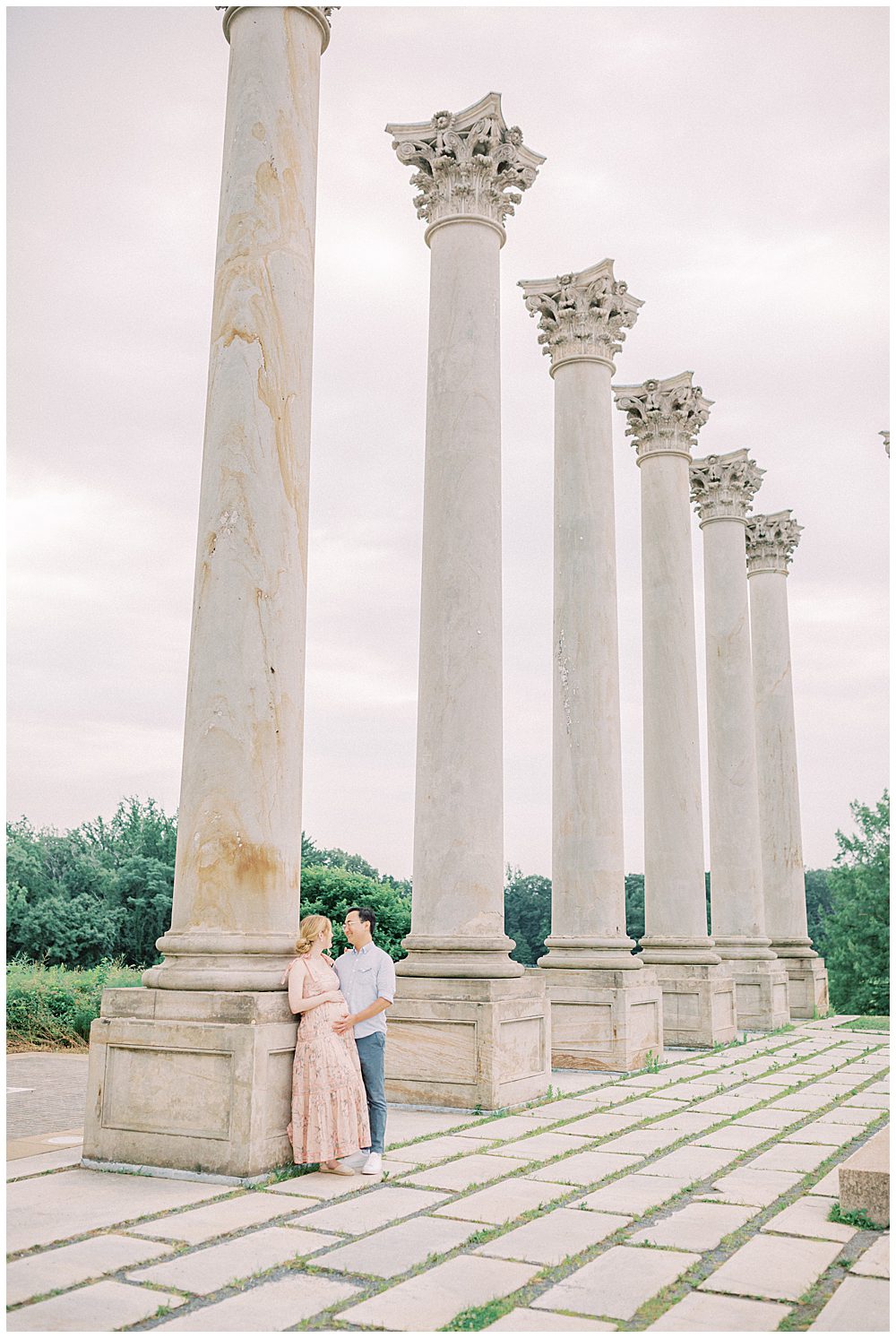 Expecting Parents Lean Against National Arboretum Columns Looking At One Another During Their Maternity Session.